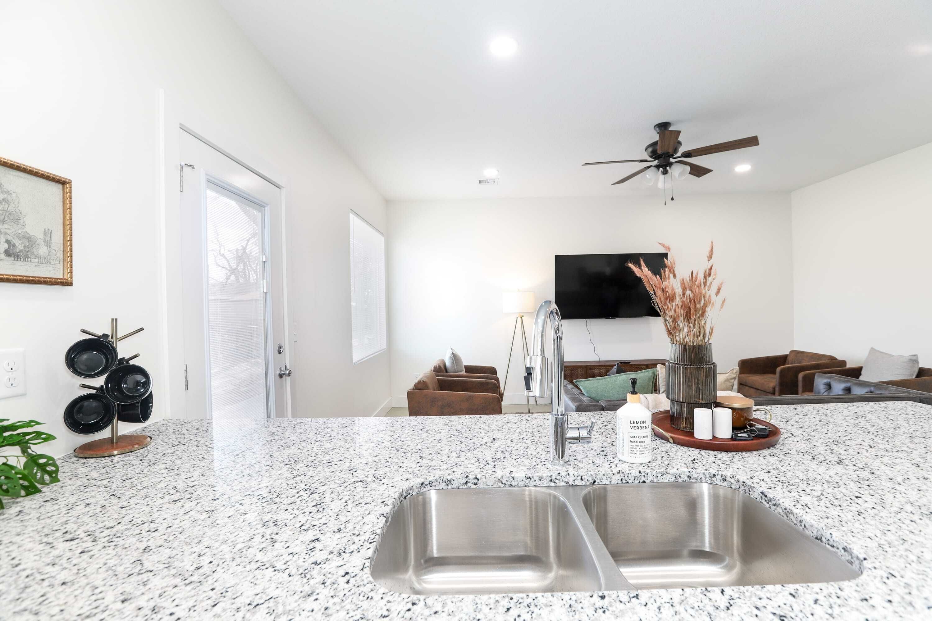 A modern kitchen with a granite countertop, stainless steel sink, and a ceiling fan.