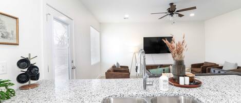 A modern kitchen with a granite countertop, stainless steel sink, and a ceiling fan.