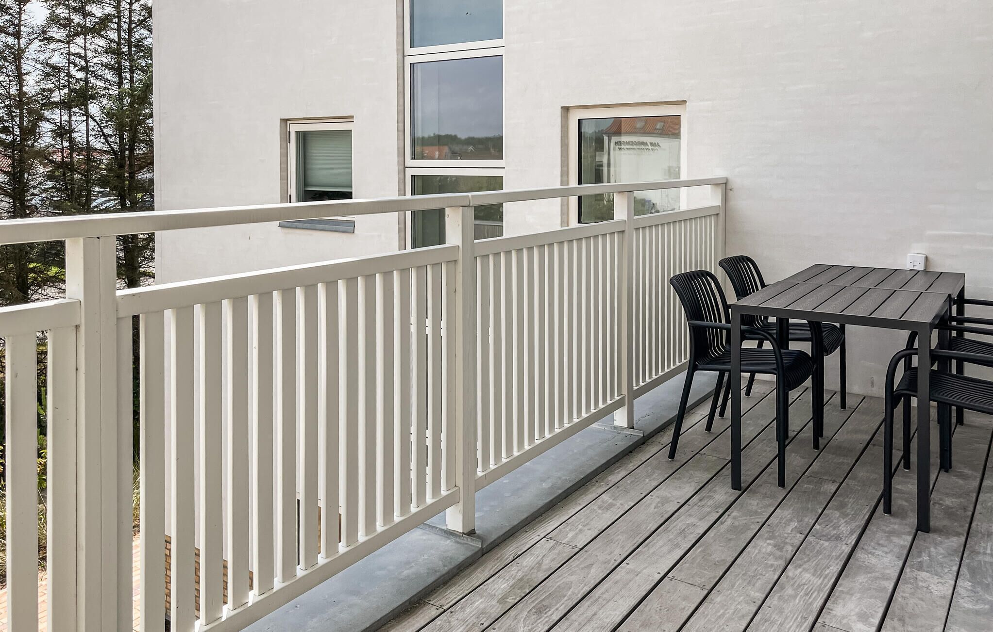 A balcony with a white railing, a table with four chairs, and a view of a building with windows.
