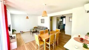 A modern living space with a dining area, a sofa, and a kitchen in the background. - 3bedroom apartment, private garden, free parking, EV charger, AC, wifi, quiet. (Toulon)