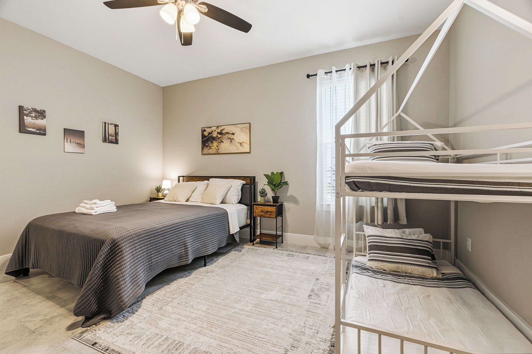 A bedroom with a bed, a nightstand, a small table with a plant, a bunk bed, and a ceiling fan.