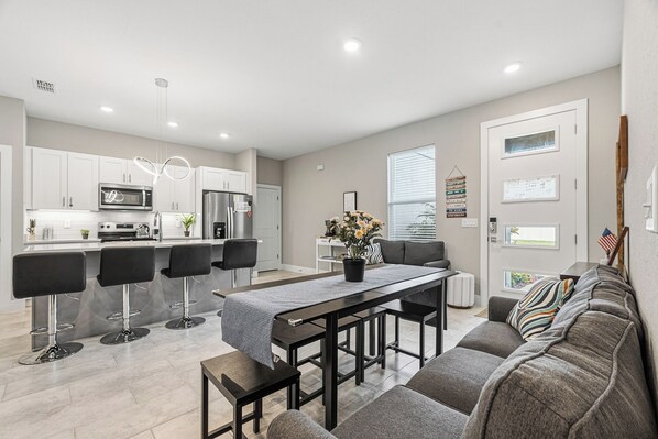 A modern kitchen with white cabinets, a dining area with a table and chairs, and a living room with a sofa and a window. - Luxury Healing Retreat North Port (North Port)