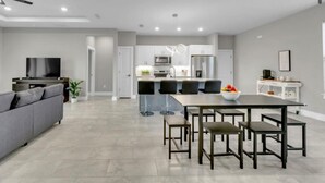 A modern living room with a gray sofa, a flat-screen TV, and a dining area with a large table and chairs.