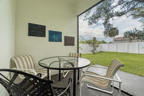 An outdoor patio with a round table and four chairs, a white fence, and a tree in the background. - Luxury Healing Retreat North Port (North Port)