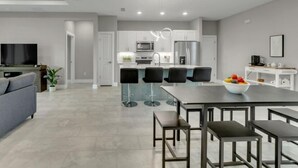 A modern kitchen with white cabinets, a stainless steel refrigerator, and a built-in oven. There is a dining area with a glass-top table and black chairs.