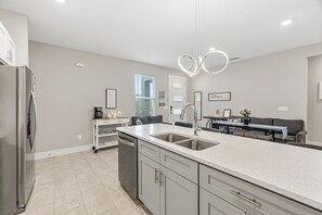 A modern kitchen with a stainless steel refrigerator, a double sink, and a dining area with a table and chairs. - Luxury Healing Retreat North Port (North Port)