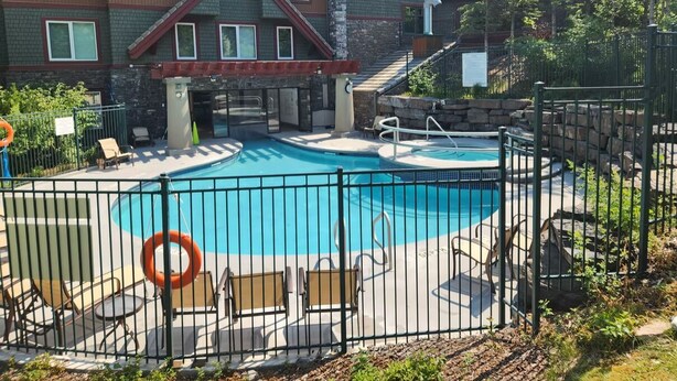 A swimming pool with lounge chairs and a lifebuoy, surrounded by a fence and a building with a stone facade.