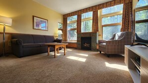 A living room with a sofa, armchair, fireplace, and large windows.