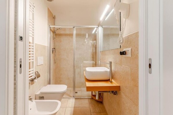 Un baño moderno con ducha de vidrio, inodoro blanco, bidet y tocador de madera con lavamanos.