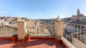 A rooftop terrace with terracotta tiles, potted plants, and a view of historic buildings and a church tower. - Residenza Già Antico Forno (Matera)