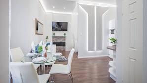 Un espace repas moderne avec une table en verre, des chaises blanches et un téléviseur à écran plat fixé au mur.