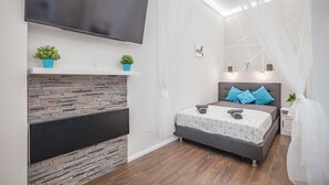 Une chambre à coucher moderne, dotée d’un téléviseur à écran plat, d’une cheminée au motif de pierres, d’un lit avec une literie aux motifs géométriques et d’une table de chevet avec une lampe.