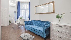 Un salon moderne avec un canapé en velours bleu, une commode blanche et un miroir au mur.