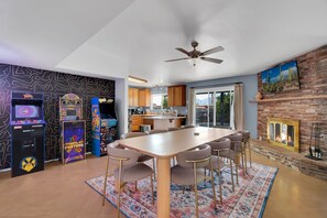 Un comedor con una mesa larga, sillas y juegos de arcade.