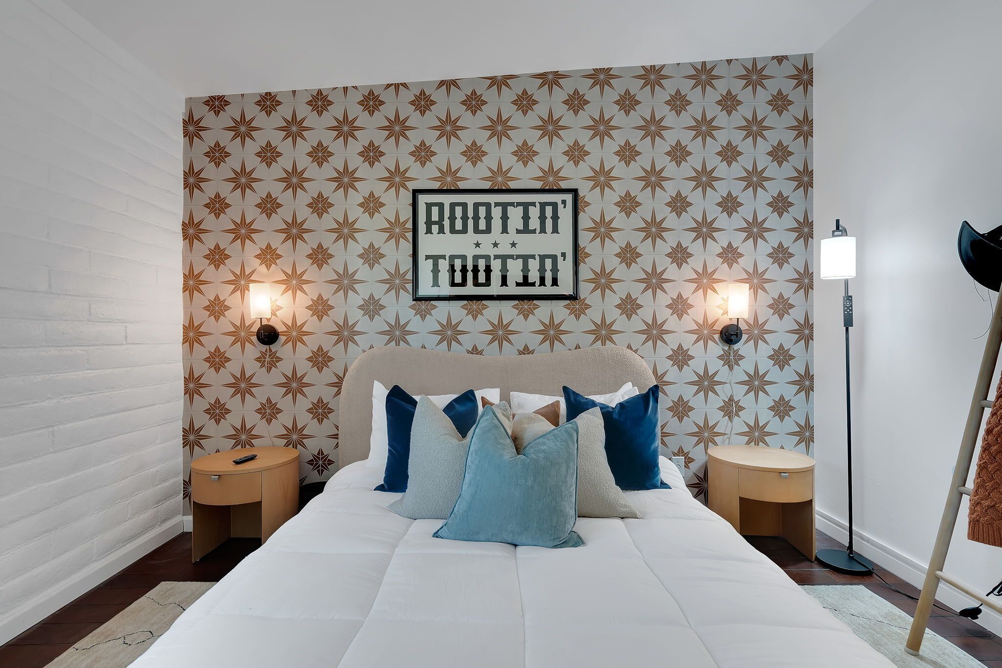 Une chambre à coucher avec un papier peint à motifs, un lit avec de nombreux coussins, des tables de chevet et une lampe sur pied.