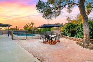 Un patio al aire libre con piscina, una zona de estar techada y una mesa con sillas.