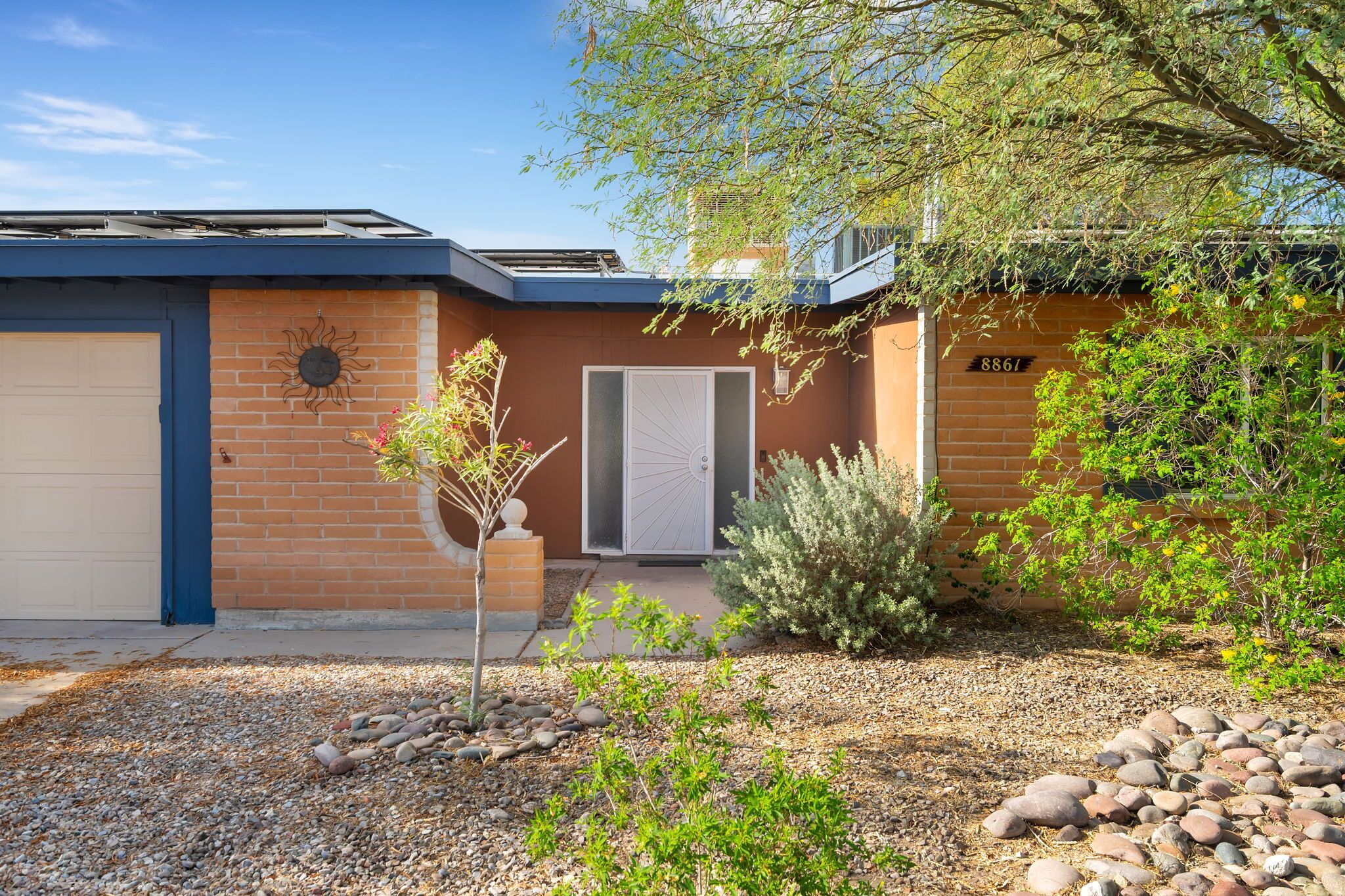 A residential building with a garage, a door with a sun design, and a mailbox.