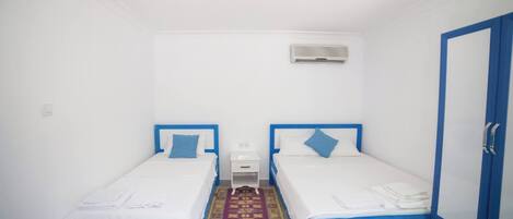 A small, clean room with two single beds, a small table, and a wardrobe.