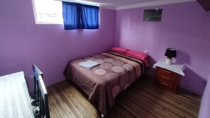 A bedroom with a bed, a nightstand, a lamp, a window with curtains, and a wall-mounted picture. - Central Department in Baños (Baños de Agua Santa)