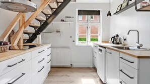 A modern kitchen with white cabinetry, a wooden staircase, and a window with a view of a brick building. - 3 bedroom lovely home in Ulfborg (Ulfborg)