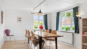 A dining area with a wooden table, six chairs, a vase with flowers, a hanging light fixture, and a window with curtains. - 3 bedroom lovely home in Ulfborg (Ulfborg)