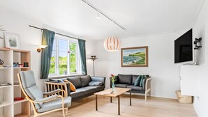 A modern living room with a sofa, armchairs, a coffee table, and a TV mounted on the wall. - 3 bedroom lovely home in Ulfborg (Ulfborg)