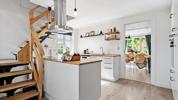 A modern kitchen with a central island, wooden staircase, and a dining area with chairs and a table. - 3 bedroom lovely home in Ulfborg (Ulfborg)
