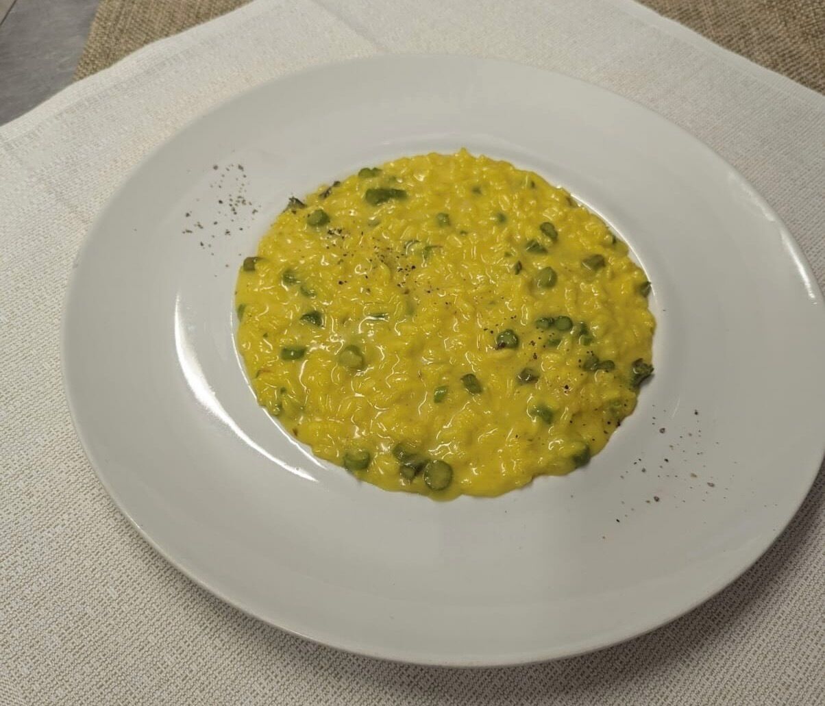 Un piatto bianco con un condimento giallo, forse una zuppa o uno stufato, guarnito con erbe aromatiche verdi.