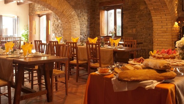 A restaurant with stone walls and wooden tables, featuring a variety of dishes and bread on the tables. - Le Case Residenza di Campagna (Assisi)
