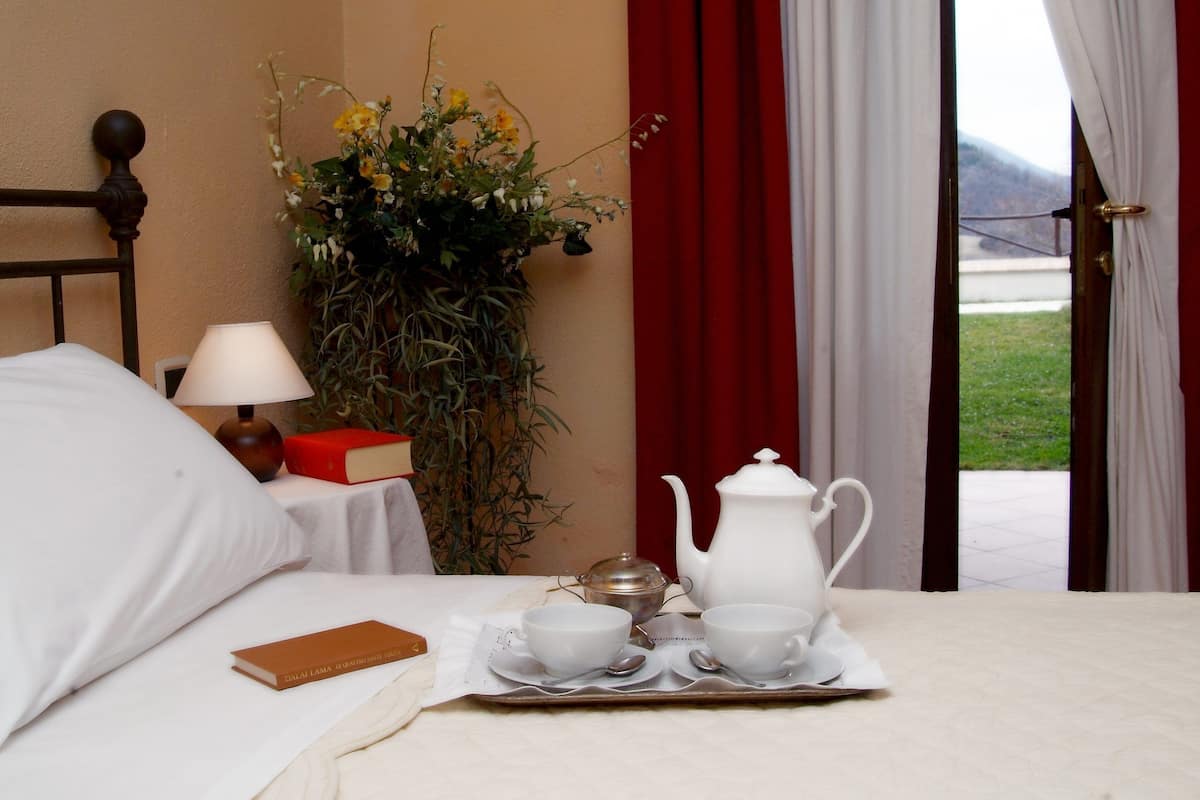 Cama bem arrumada com bandeja de chá, um livro e um vaso de flores.