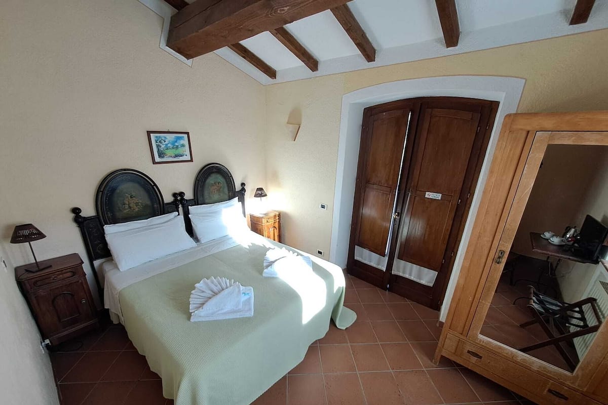 Quarto com cama, cabeceira de madeira, mesa de cabeceira, abajur, quadro na parede e guarda-roupa com espelho.