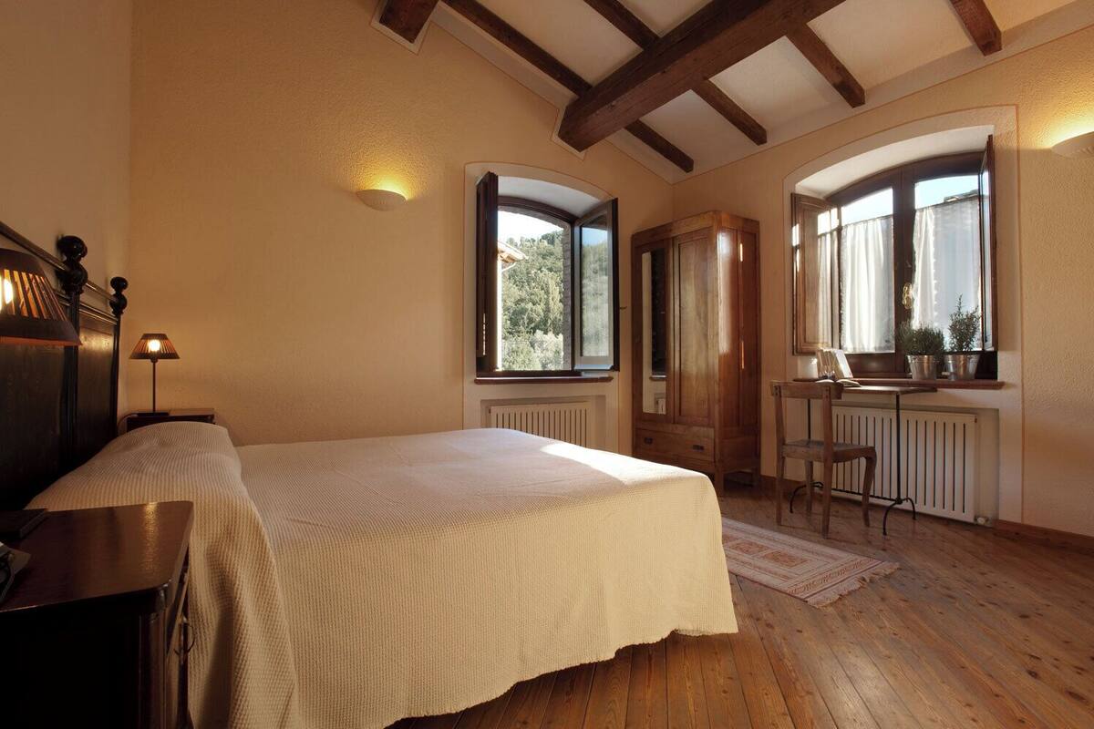 Quarto com cama, escrivaninha e duas janelas.