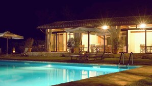 A nighttime pool area with a covered seating area, lounge chairs, and a pool. - Le Case Residenza di Campagna (Assisi)