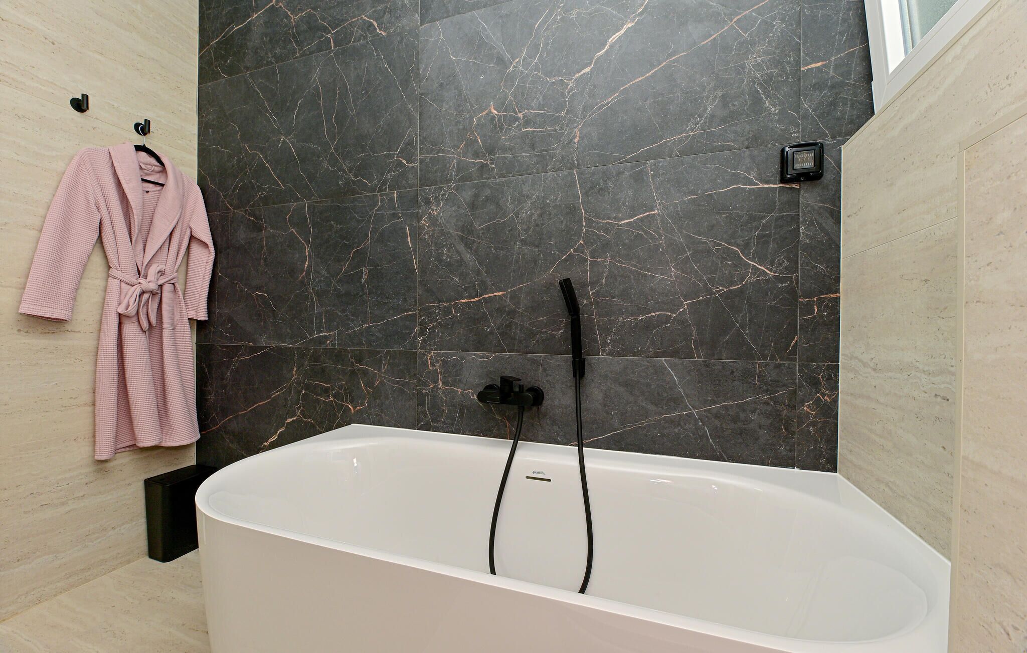 A modern bathroom with a freestanding bathtub, marble walls, and a towel rack with a pink robe.