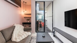 A modern living room with a grey sofa, a white fluffy throw, a black coffee table, and a flat-screen TV mounted on the wall. - Flamingo - Sea Point Lions View (Cape Town)
