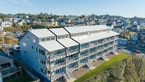 A modern multi-story building with a flat roof, large windows, and a central staircase. - Large Oceanfront Views 2 Kings Bed 2 Bath Lg Spa Tub Romantic Nye Beach Getaway (Newport)