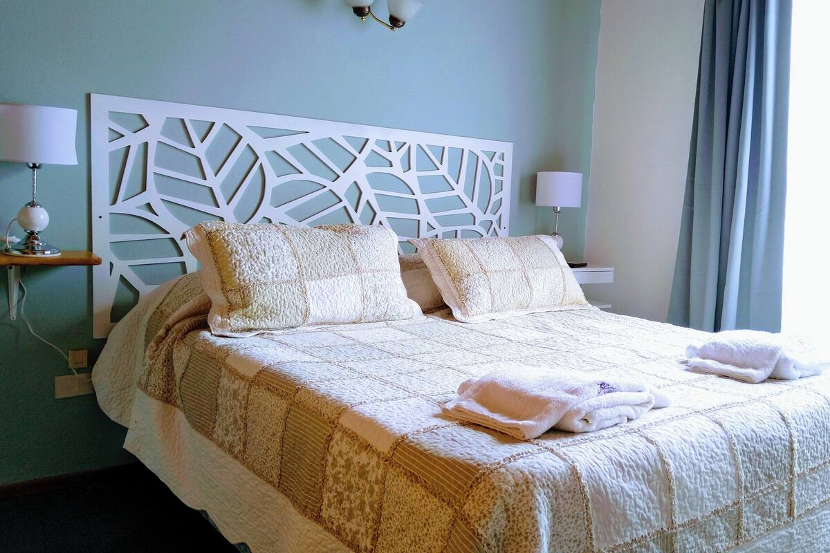 Un lit bien fait, avec une couvre-lit matelassé, deux oreillers et deux serviettes pliées.