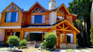 A wooden house with a stone chimney, large windows, and a sign that reads "Sonado". - Costa Soñada (San Martín de los Andes)