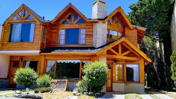 Une maison en bois avec une cheminée en pierre, de grandes fenêtres et une enseigne sur laquelle on peut lire « Sonado ».