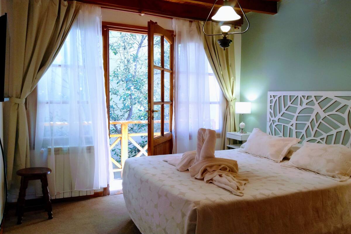 Une chambre à coucher avec un lit, une table de chevet, une lampe et une vue sur l’extérieur.