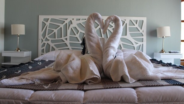 A bed with towels arranged in a heart shape, a white headboard, and bedside lamps. - Costa Soñada (San Martín de los Andes)