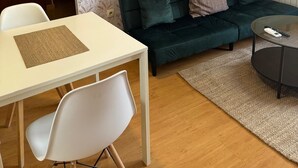 Una sala de estar con un sofá verde, una mesa blanca con un mantel individual, una silla blanca y una mesa de centro redonda.