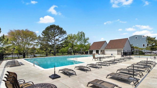 A pool area with lounge chairs and a building in the background. - Spring Lake 504 (Rehoboth Beach)