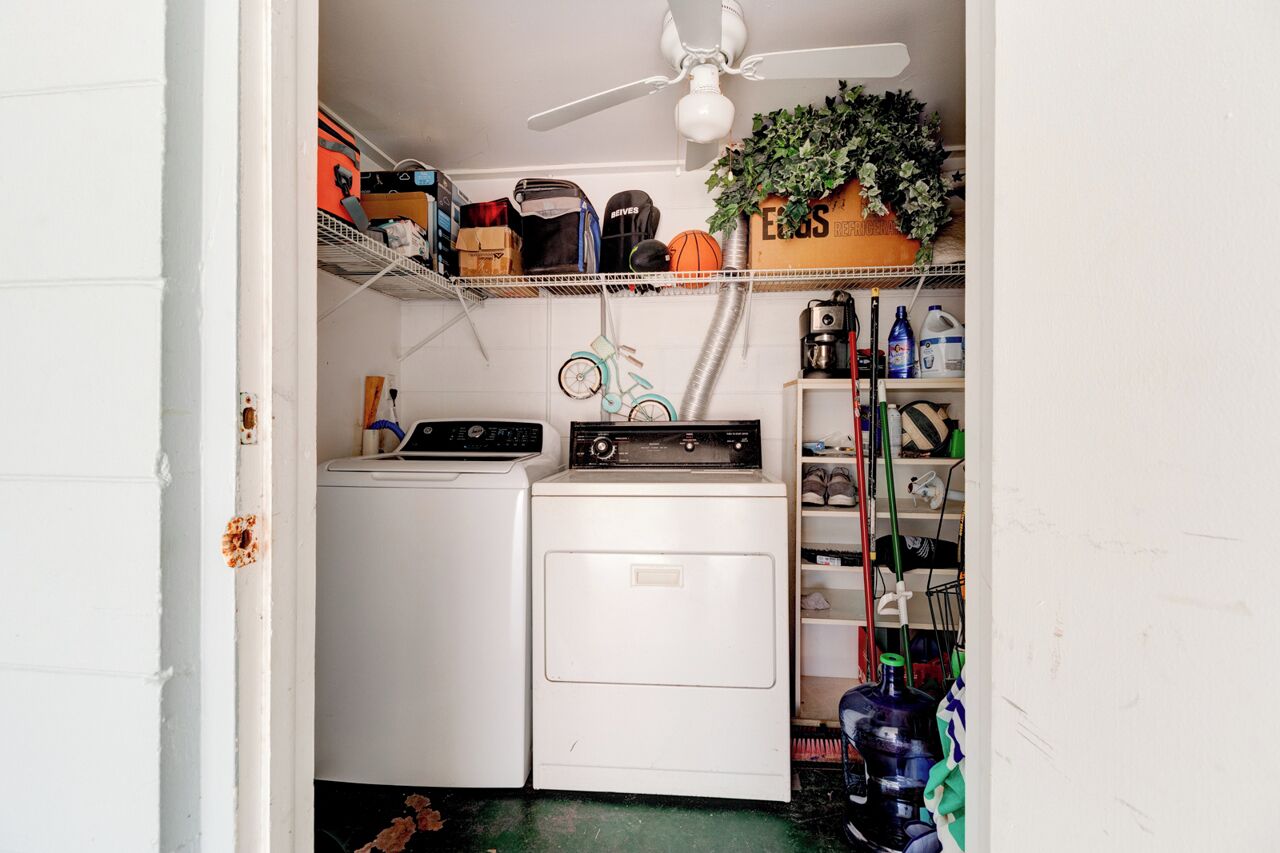 A laundry room with a ceiling fan, washing machine, dryer, shelves with various items, and a bicycle.
