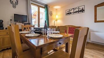 Un coin repas avec une table en bois dressée pour quatre personnes, un téléviseur et une lampe.