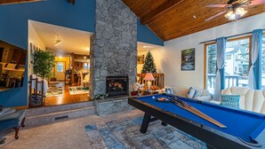 Een gezellige woonkamer met een pooltafel, een stenen open haard en een groot raam met gordijnen.