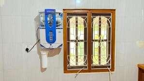 Ein Zimmer mit einem Fenster mit Gitterstäben, einem blauen Wasserspender und einer weißen Steckdose.