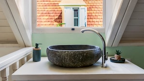 Un baño con un lavabo de piedra, un grifo, un dispensador de jabón y una pequeña planta en maceta.