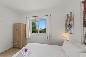 Quarto com cama, guarda-roupa de madeira, janela com cortinas, luminária na parede e quadro decorativo.