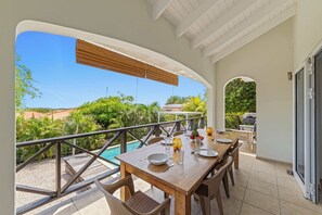 Uma área de refeições ao ar livre com vista para uma piscina e vegetação exuberante.